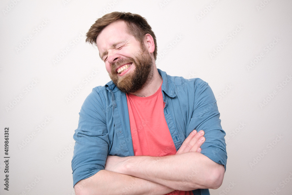 Funny shy man stands with crossed arms and smiles cute with eyes closed. White background. Funny shy man stands with crossed arms and smiles cute with eyes closed. White background.