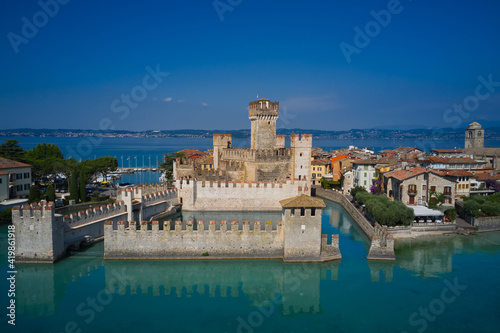 Sirmione, Lake Garda, Italy. The famous Sirmione Castle. Frontal close aerial view. Reflections of the castle in the water in the background blue sky