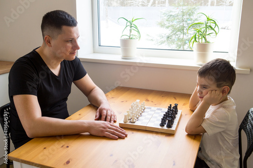 A father and a preschooler are going to play chess. The boy is bored