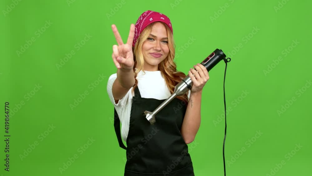 Young blonde girl using hand blender smiling and showing victory sign with a cheerful face over isolated background on green screen chroma key Young blonde girl using hand blender smiling and showing victory sign with a cheerful face over isolated background on green screen chroma key