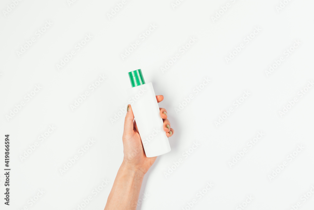 Female hand holding blank bottle of cosmetic product lotion with green cap Female hand holding blank bottle of cosmetic product lotion with green cap