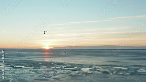 Beautiful drone shot of kite boarding over frozen sea at sunset. Camera follows a kite, flies over broken pieces of ice and open water. 4k footage