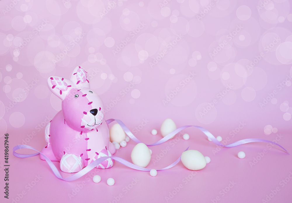 The pink bunny with white chocolate eggs and purple ribbon on pink background with bokeh effect The pink bunny with white chocolate eggs and purple ribbon on pink background with bokeh effect