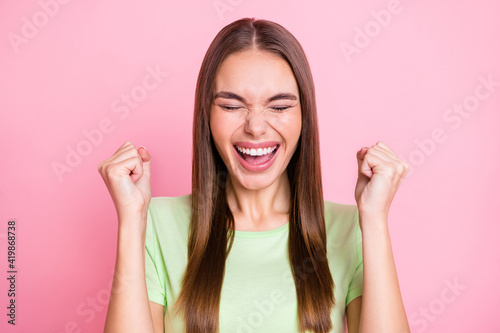 Photo of impressed lucky young lady wear green t-shirt rising fists closed eyes isolated pastel pink color background