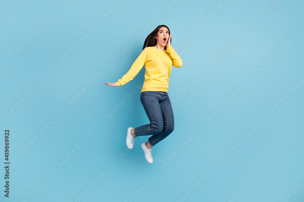 Full size photo of nice stressed brunette long hairdo lady jump wear shirt jeans sneakers isolated on blue color background Full size photo of nice stressed brunette long hairdo lady jump wear shirt jeans sneakers isolated on blue color background