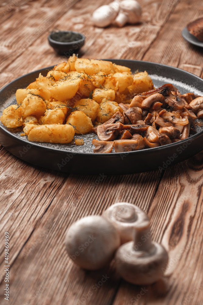 Fried potatoes with mushrooms on a wooden rustic table near fresh mushrooms Fried potatoes with mushrooms on a wooden rustic table near fresh mushrooms