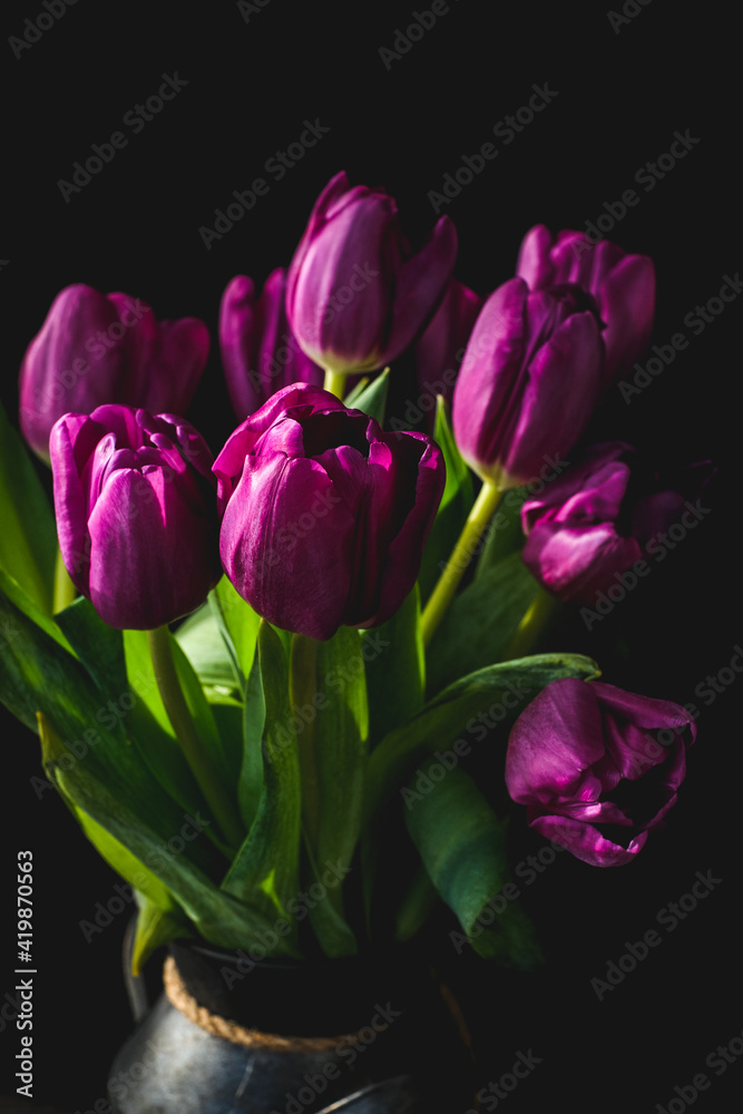 Lilac purple tulip flowers on table. Spring bouquet flowers in vintage vase. Floral concept. Floral background. Dark black background.