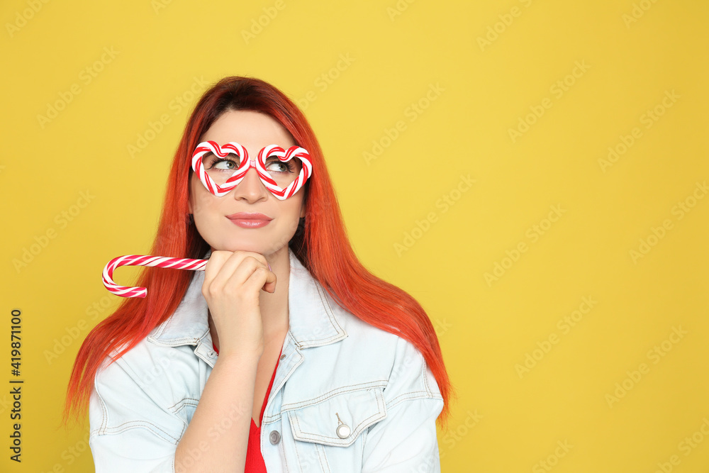 Young woman with bright dyed hair holding candy canes on yellow background. Space for text Young woman with bright dyed hair holding candy canes on yellow background. Space for text