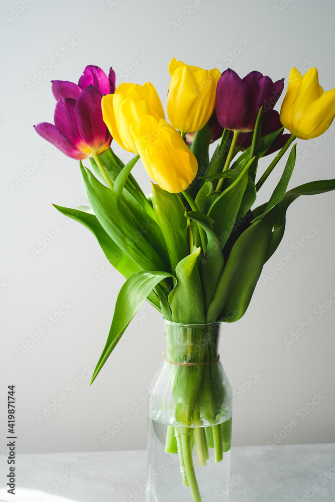 Lilac purple tulip flowers on table. Spring bouquet flowers in vintage vase. Floral concept. Floral background. White decoration and light background Lilac purple tulip flowers on table. Spring bouquet flowers in vintage vase. Floral concept. Floral background. White decoration and light background