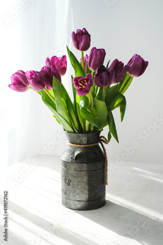 Lilac purple tulip flowers on table. Spring bouquet flowers in vintage vase. Floral concept. Floral background. White decoration and light background