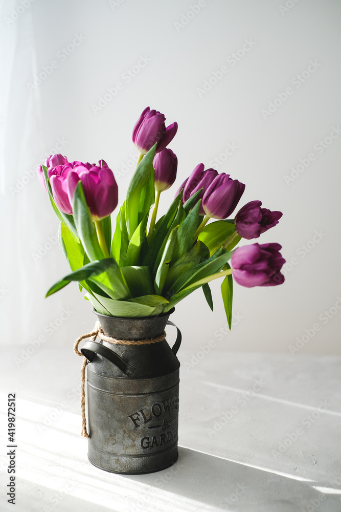 Lilac purple tulip flowers on table. Spring bouquet flowers in vintage vase. Floral concept. Floral background. White decoration and light background Lilac purple tulip flowers on table. Spring bouquet flowers in vintage vase. Floral concept. Floral background. White decoration and light background