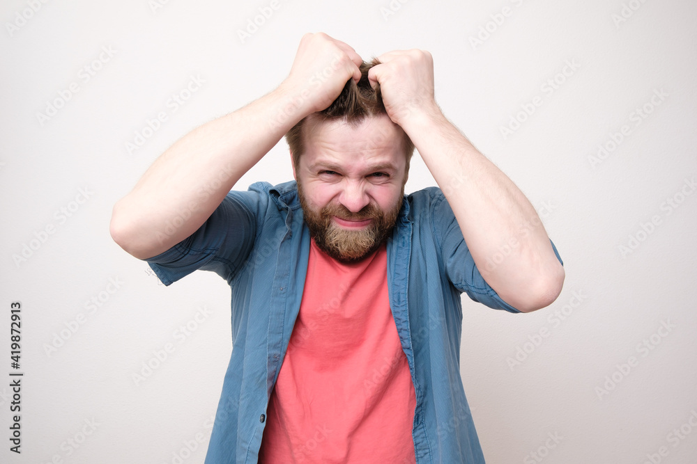 Caucasian man in stress, he is nervous, holding hair with hands and looking at the camera. White background. Caucasian man in stress, he is nervous, holding hair with hands and looking at the camera. White background.