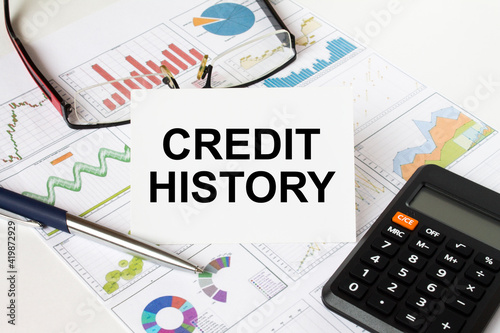White card with text Credit History it is lies on financial charts with a calculator and eyeglasses
