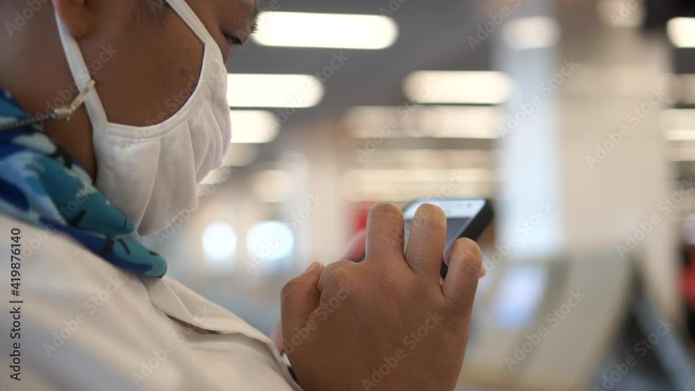 Asian Senior Traveler with New Normal in protecting face mask using smartphone for online social media reading news and searching check in flight timetable at airport terminal. Safe travel in COVID-19 Asian Senior Traveler with New Normal in protecting face mask using smartphone for online social media reading news and searching check in flight timetable at airport terminal. Safe travel in COVID-19