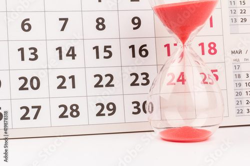 Time passing concept. Crystal hourglass with red sand and calendar on light background