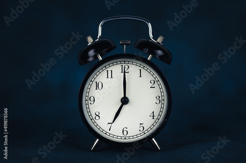 The time is seven o'clock in the morning. Time - 07-00. Retro clock. Dark background. Lifting concept for work. Copy space and cut out.