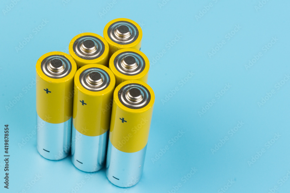 Photo of gray-yellow alkaline AA batteries on blue background. Recycling of rechargeable NiMH batteries. The most popular size of accumulators. Copy space. Photo of gray-yellow alkaline AA batteries on blue background. Recycling of rechargeable NiMH batteries. The most popular size of accumulators. Copy space.