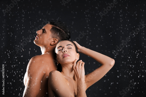 Couple taking shower against black background. Woman washing hair