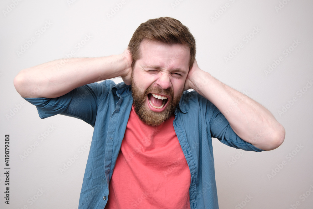Caucasian man in stress, he is tired of the noise, covers ears with hands and shouts loudly. Psychological health concept. Caucasian man in stress, he is tired of the noise, covers ears with hands and shouts loudly. Psychological health concept.