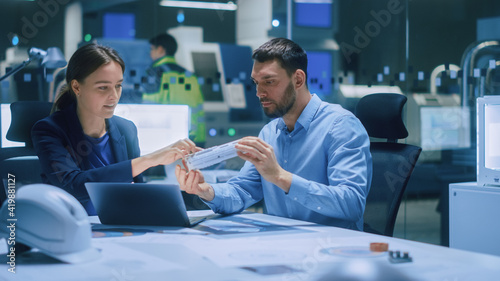 Industry 4.0 Modern Factory Meeting Room: Chief Engineer Holds Mechanism, Shows it to Female Designer, They Talk. Scientists in Contemporary Lab Build Electronic Machinery for With Futuristic Design