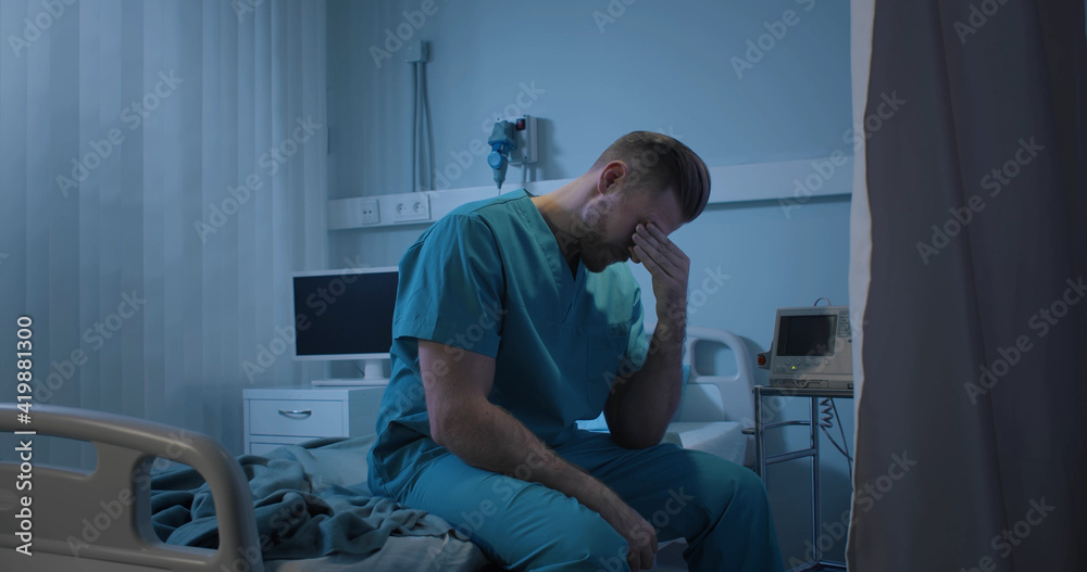Upset and tired doctor sitting on empty stretcher bed