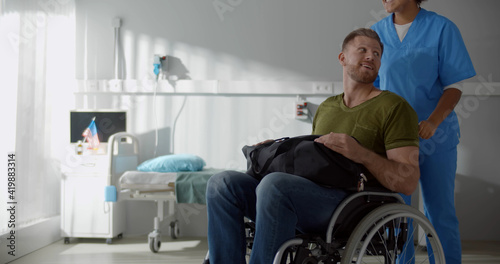 Canvas-taulu Afro female nurse talking to discharged male patient in wheelchair and smiling