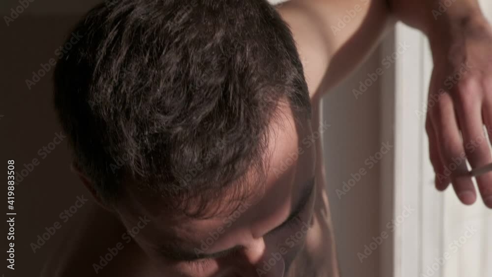 Close-up young muscular man smoking a cigarette and looks out the window, slow motion Close-up young muscular man smoking a cigarette and looks out the window, slow motion