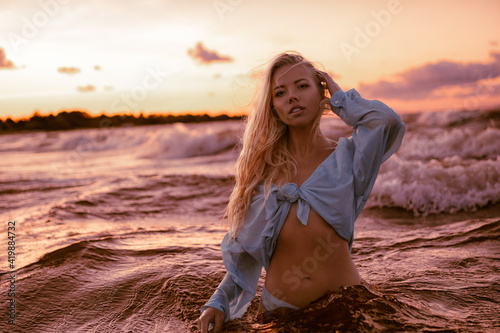 Young beautiful adult sexy blonde model pose in the wet shirt by swimming and taking fun at dramatic sunset