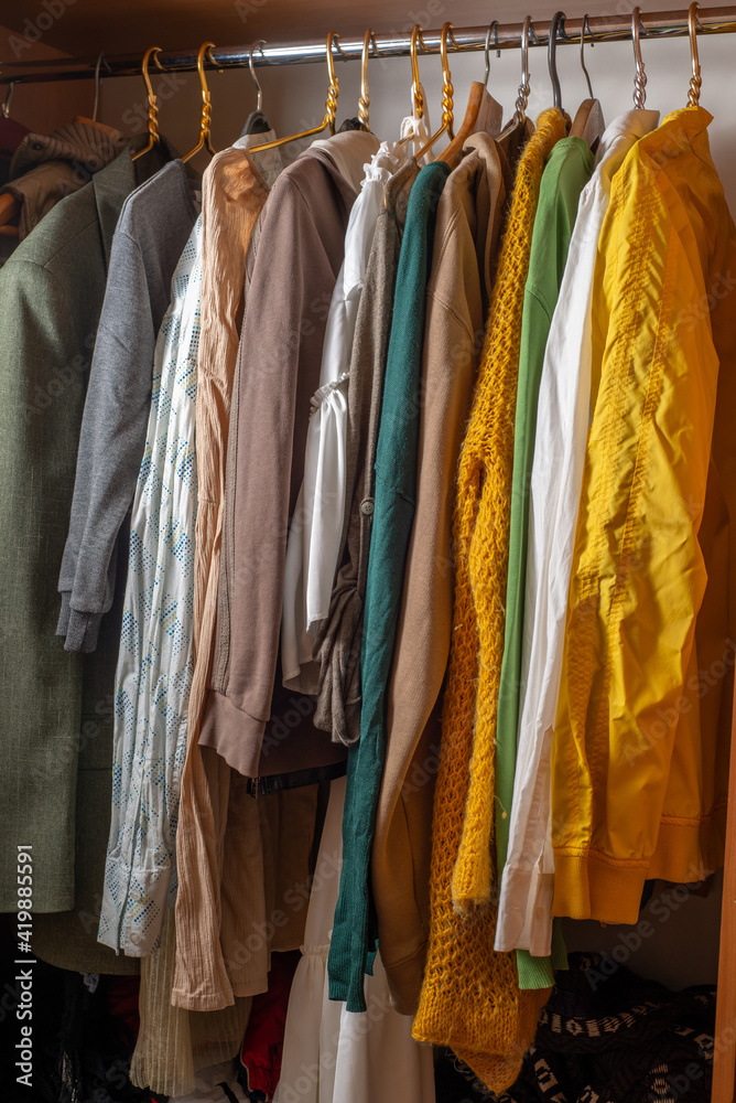 Lots of brightly colored clothes on hangers in the closet. Decluttering the cabinet. Second hand