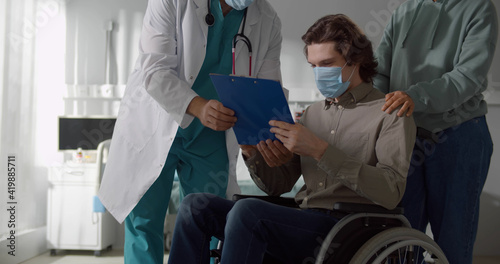 Male patient sitting in wheelchair and wearing safety mask signing discharge paper in hospital