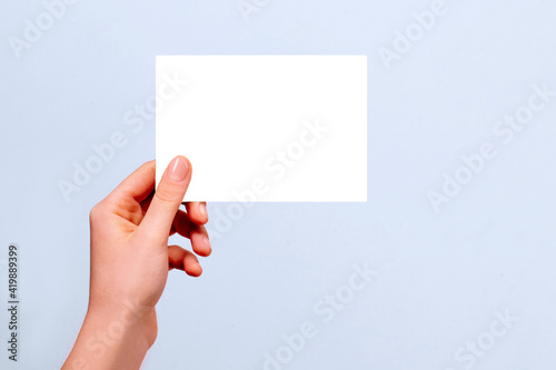 female hand holding white card mockup on gray background