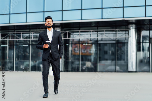 Fototapeta An Indian man in a black suit, a successful manager walks down the street of a m