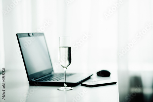 Laptop and glass of champagne on white table at home kitchen, work from home