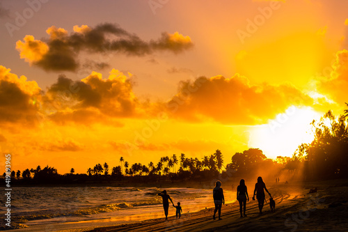 Pessoas caminham durante pôr do sol na praia.