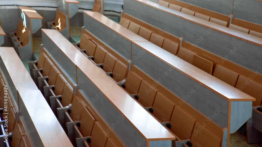 Modern desks in lecture hall. Rows of long wooden tables with vacant seats in the light auditorium at university. Classroom without students. Modern desks in lecture hall. Rows of long wooden tables with vacant seats in the light auditorium at university. Classroom without students.