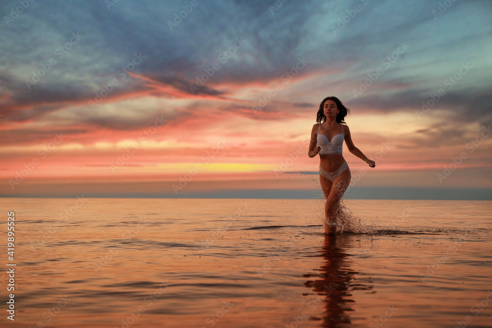 Young beautiful sexy fit lingerie brunette  model running in the water at dramatic sunset 