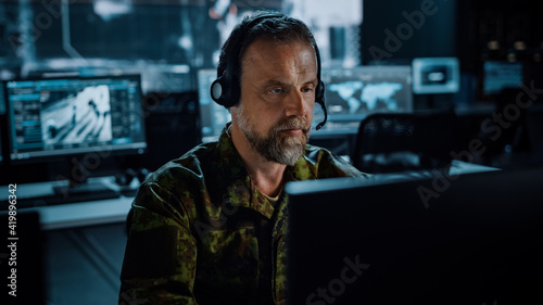 Bearded Military Surveillance Officer in Headset Working in a Central Office Hub for Cyber Operations, Control and Monitoring for Managing National Security, Technology and Army Communications.