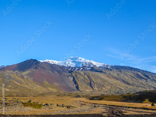 Autumn vibes in the grassland. Grass and bushes turned gold. Bright sun makes them shine. In the back a volcano and higher glaciers hiding behind the thick clouds. Beauty of the nature.