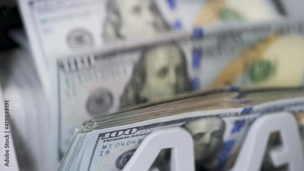 Money counting equipment for paper money calculation. Automatic mechanism for bank financial operations. Female hand taking a bundle of counted dollar bills from counting machine. Close-up.