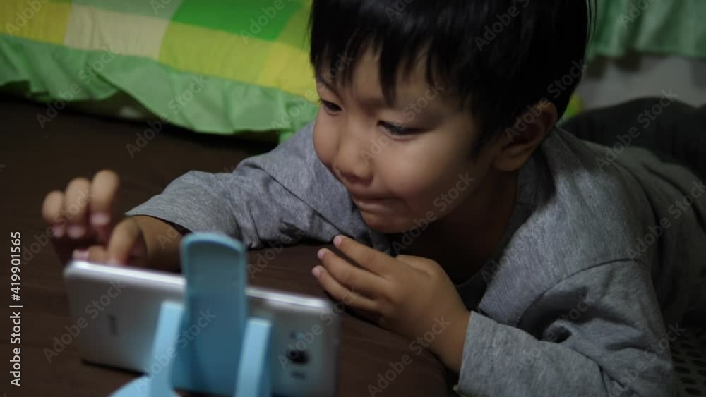 4K Asian child boy lying on bed, hand touch screen, watching video on smartphone, sneeze from dust allergy in room. Concept of technology, communication, health care.