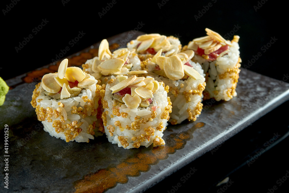 Delicious crispy sushi roll with tuna, peanuts, popcorn and cucumber, served on a ceramic plate with ginger and wasabi. Isolated on a black background. Japanese food Delicious crispy sushi roll with tuna, peanuts, popcorn and cucumber, served on a ceramic plate with ginger and wasabi. Isolated on a black background. Japanese food