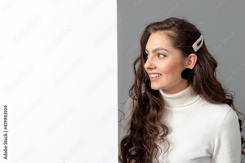 beautiful sensual woman with long curly hair shows a blank banner, isolated on gray, copy space beautiful sensual woman with long curly hair shows a blank banner, isolated on gray, copy space