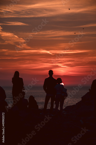 Group of people silhouette admiring a beautiful red and orange sunset in a famous sunset point in Sardinia, Italy. Somebody taking pictures, somebody taking a selfie. Summer feeling. © laura