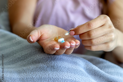 Cropped shot of a young woman taking medication at home. Sick women feeling bad and taking pills while spending time at home. Depressed girl holds antidepressant meds, painkiller for menstrual pain.