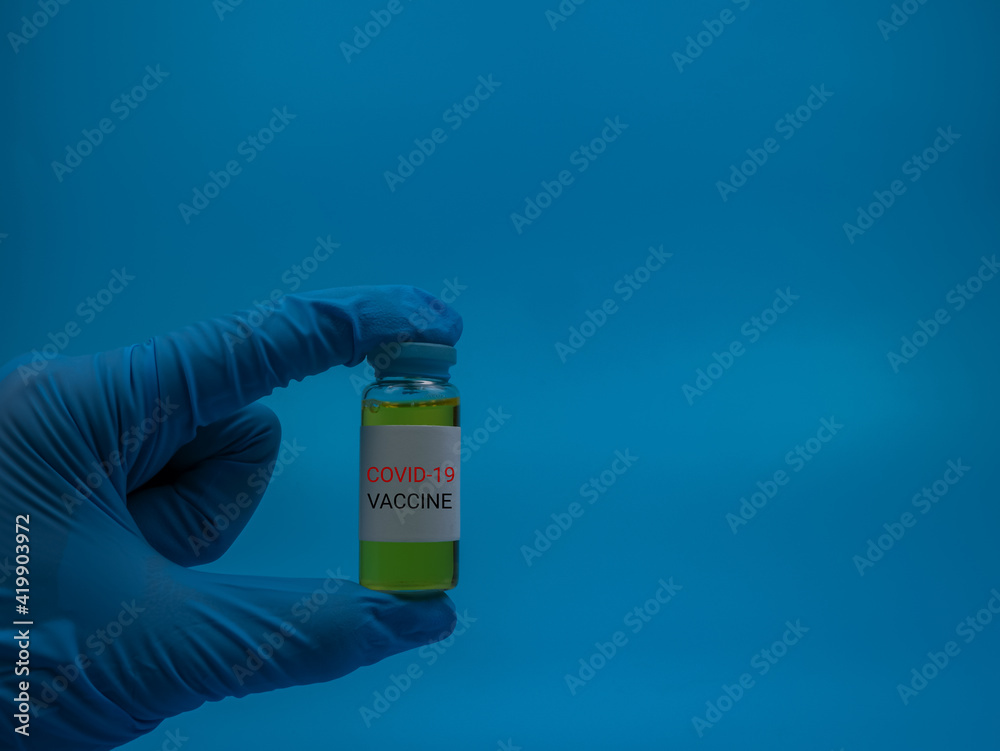 An image of person holding vial covid-19 vaccine isolated on a blue background. Healthcare and medical concept. Selective focus image. An image of person holding vial covid-19 vaccine isolated on a blue background. Healthcare and medical concept. Selective focus image.