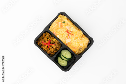 Top view of thai food, spicy curry pork with cucumber and friend egg in black contain box isolate in white.
