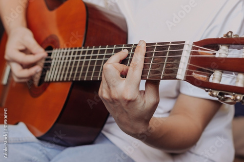 Close up of hand of young woman in the white t-shirt and blue jeans playing acoustic guitar. Girl picks a barre chord clamping frets on the fretboard