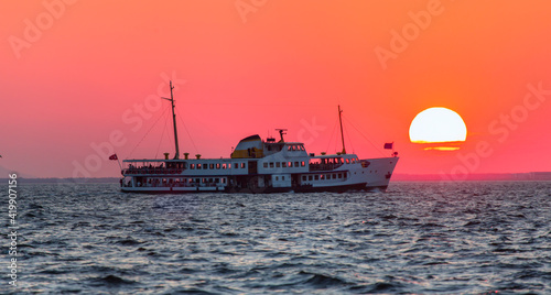 Water trail foaming behind a passenger ferry boat in the Gulf of Izmir at red sun - Izmir, Turkey © muratart