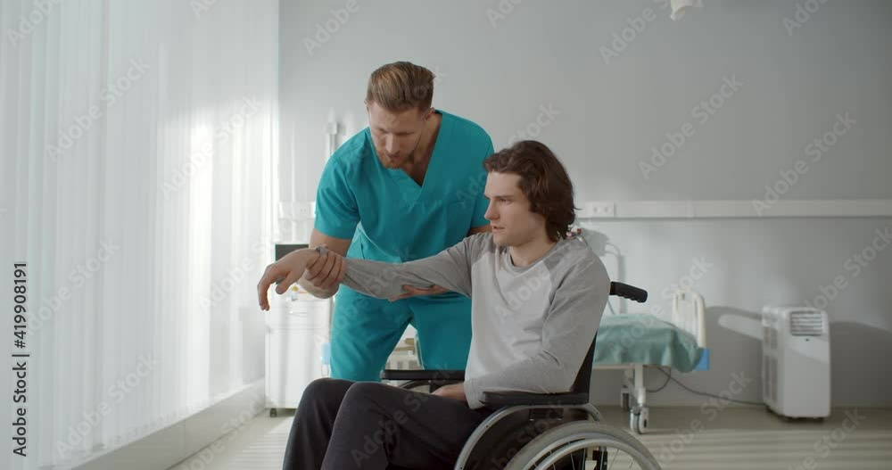 Nurse lifting arm of young paralyzed man sitting in wheelchair Nurse lifting arm of young paralyzed man sitting in wheelchair