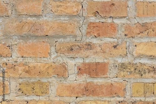 Symmetrical brick wall background. Red and brown colored terracotta bricks from an abandoned house, some clean, some dirty. Cracks in the wall.
